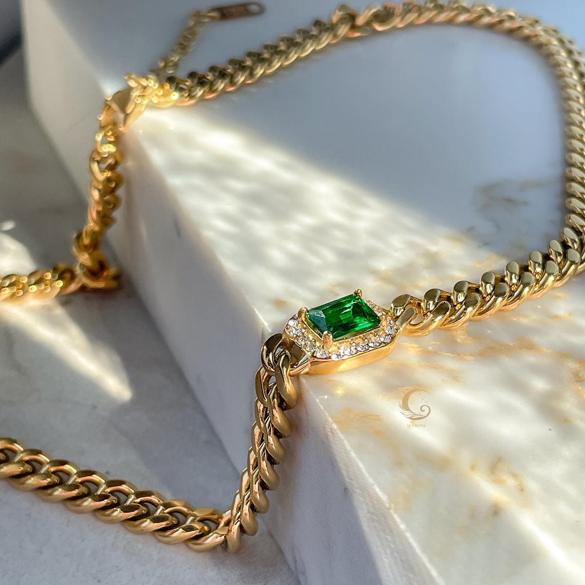 Close-up of Harper Cuban Chain Necklace with green crystal and zirconia, displayed on marble surface in warm sunlight.