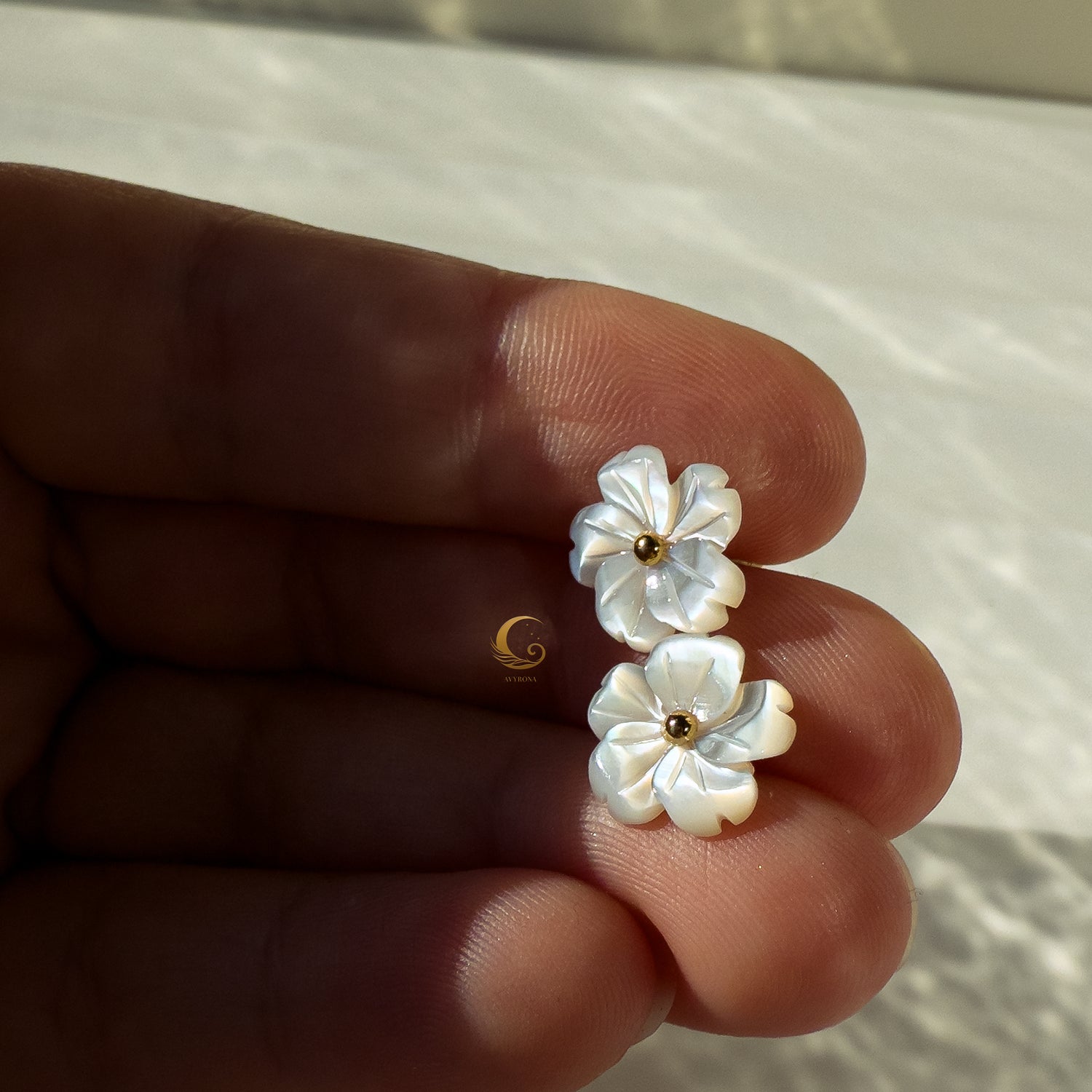 Imira shell flower stud earrings held in fingers, showing gold center and natural shimmer