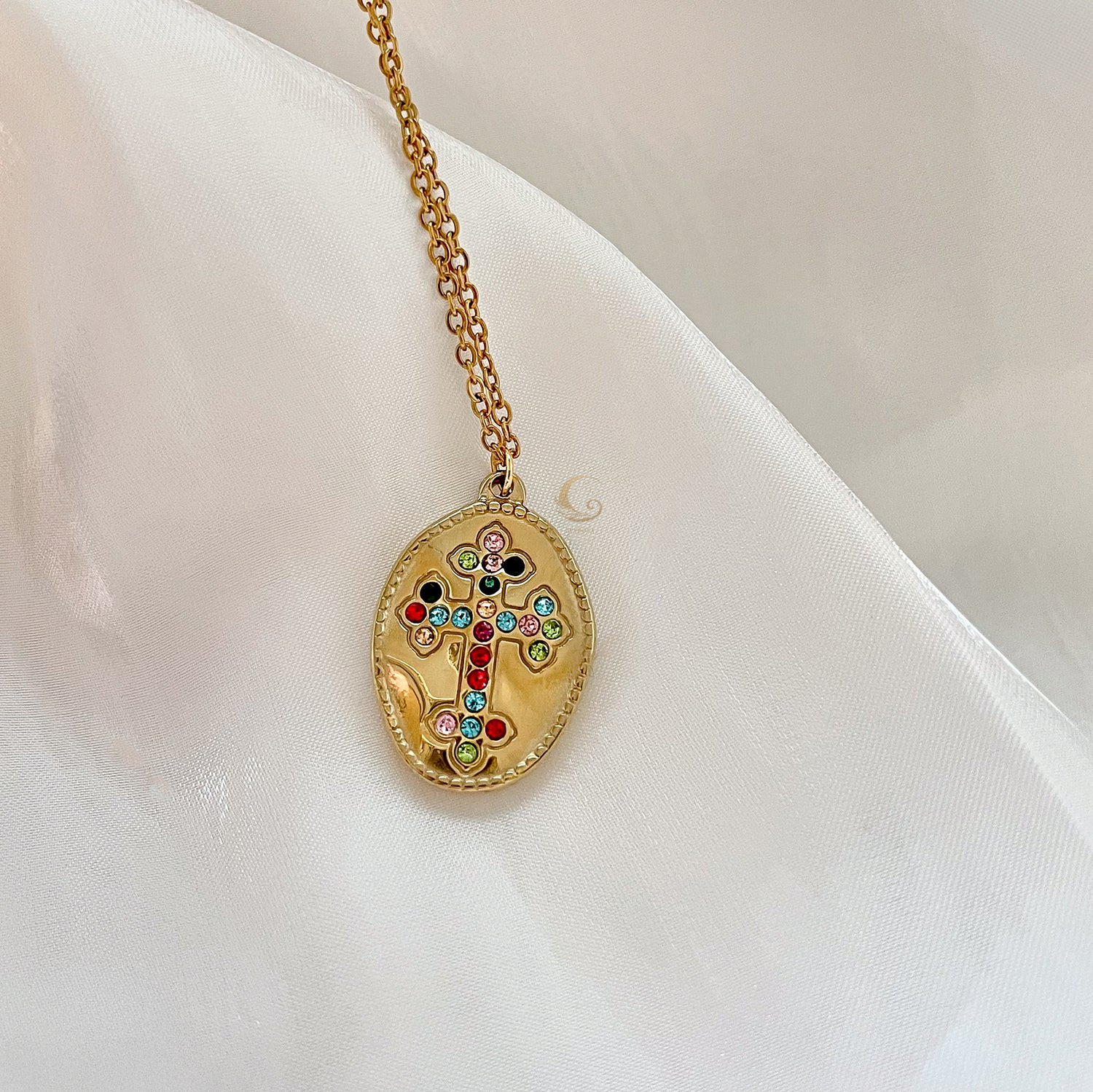  Isadora cross necklace on satin fabric, showing multicolored cubic zirconia details.