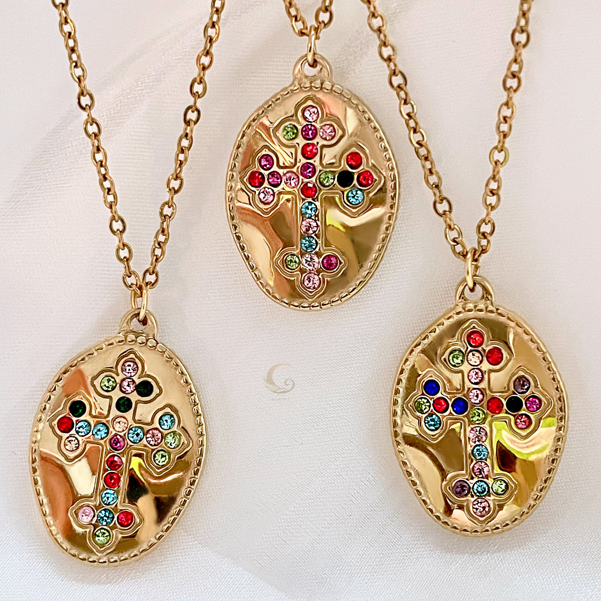  Three gold medallion necklaces with colorful cubic zirconia crosses displayed on light fabric.