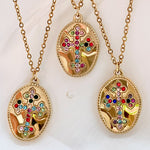  Three gold medallion necklaces with colorful cubic zirconia crosses displayed on light fabric.