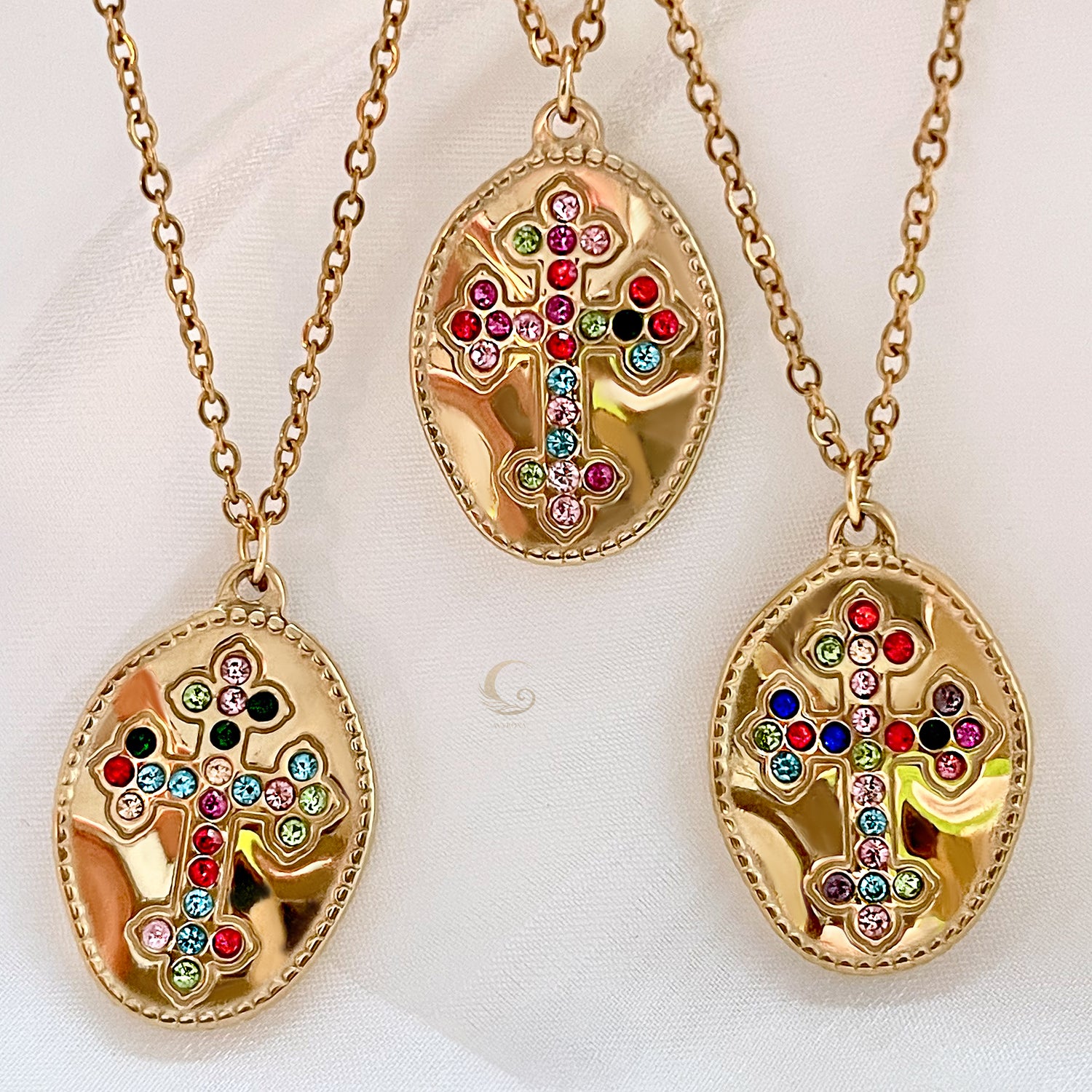  Three gold medallion necklaces with colorful cubic zirconia crosses displayed on light fabric.