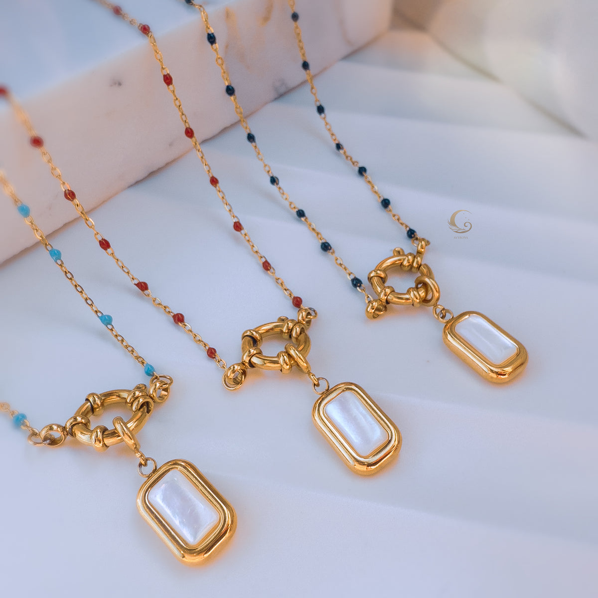 Group of four Liora necklaces in different beading colors—sky blue, red, navy, and turquoise—each with gold toggle clasps and mother of pearl pendants.