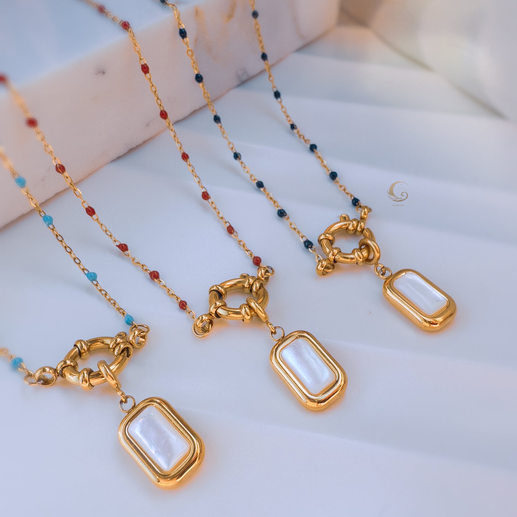 Group of four Liora necklaces in different beading colors—sky blue, red, navy, and turquoise—each with gold toggle clasps and mother of pearl pendants.