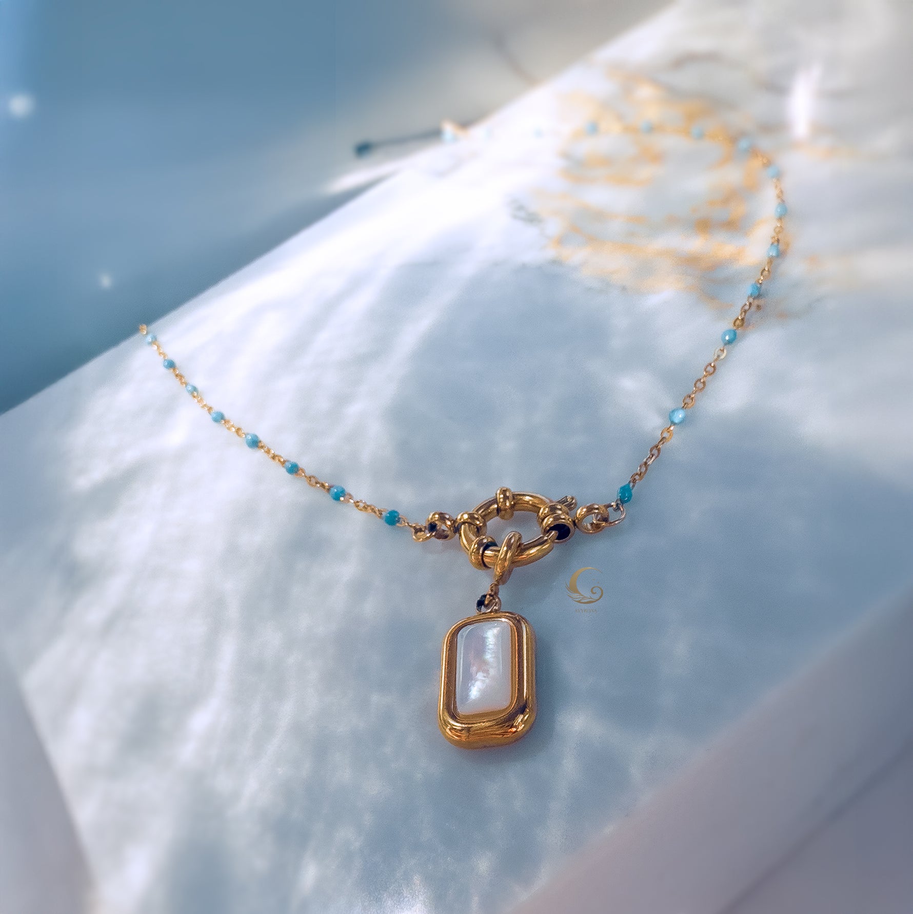 Close-up of the Liora necklace with sky blue beaded chain and rectangular mother of pearl pendant on a soft marble background, highlighting its delicate toggle clasp.