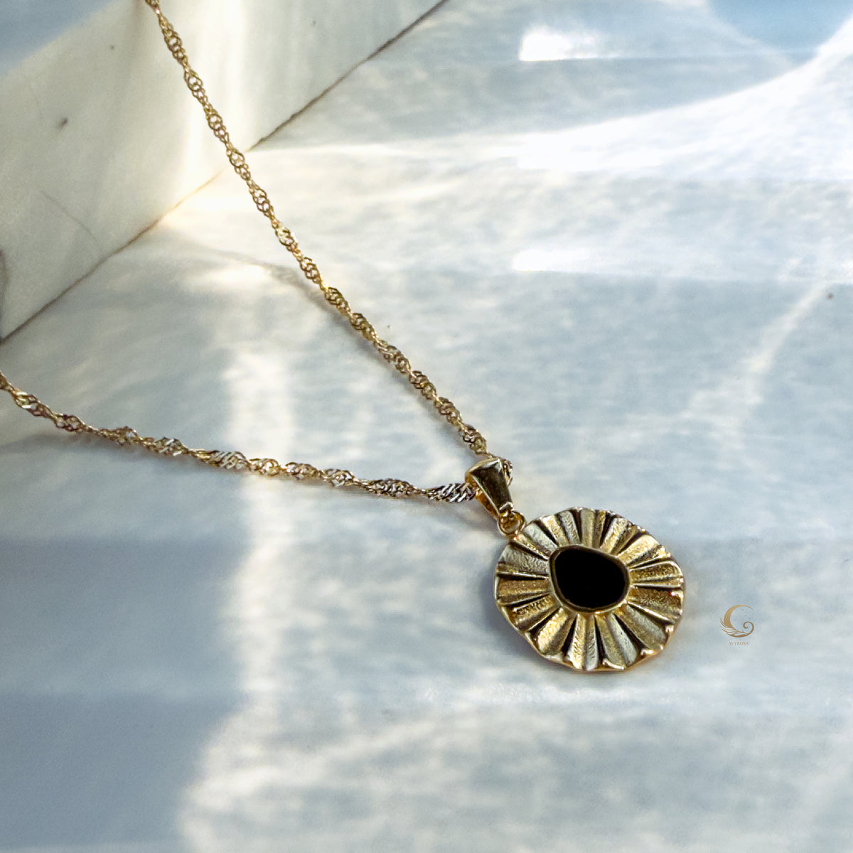 Liore Black Flower Necklace displayed flat on white silk fabric, twisted gold chain with black enamel flower pendant.