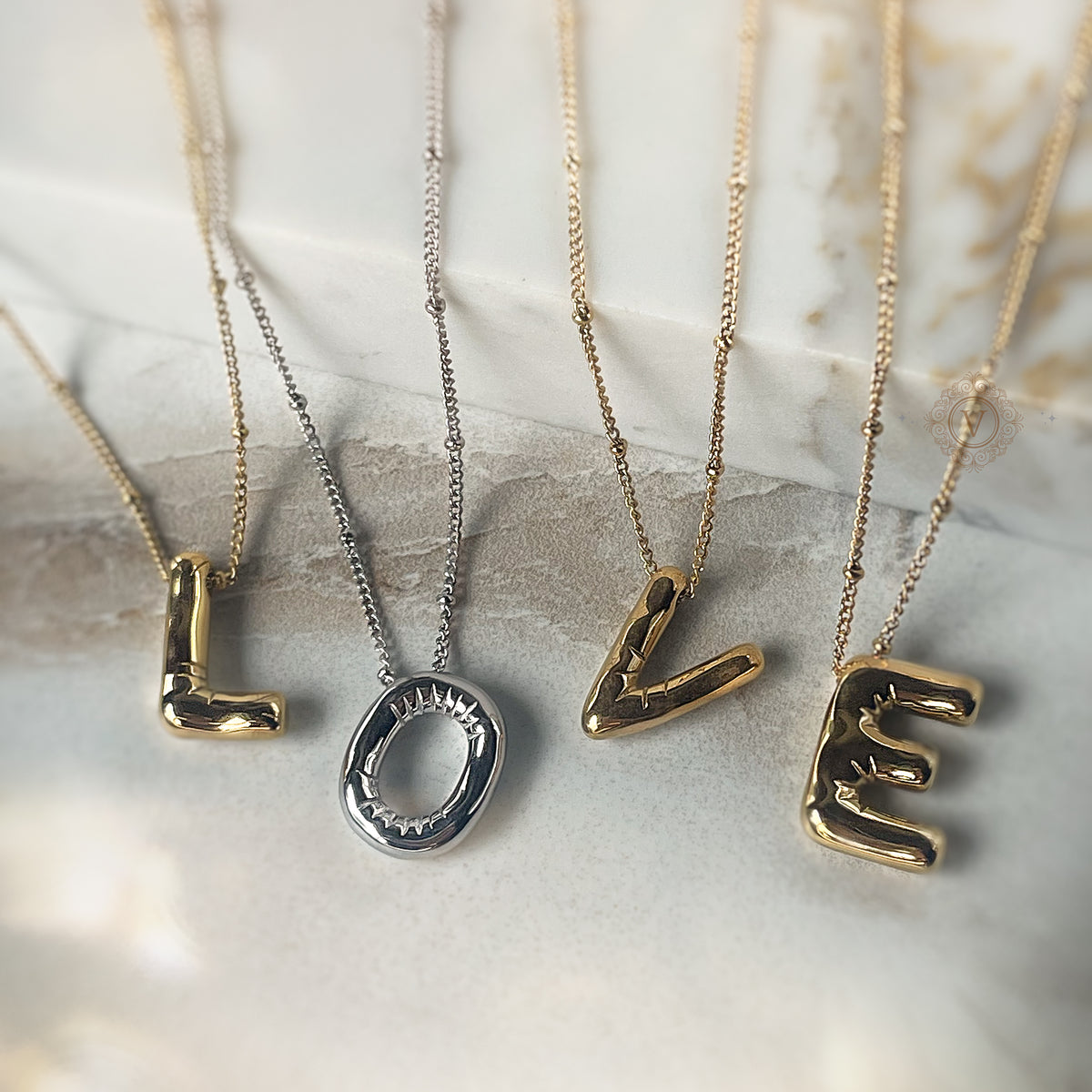 LOVE balloon letter necklaces in alternating gold and silver tones laid flat on a marble background.