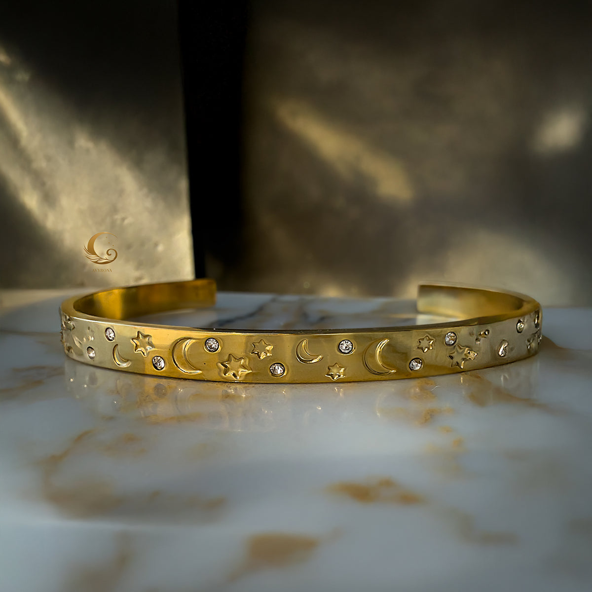 Celestial gold bracelet with moon and star symbols, captured in front-facing view with warm ethereal glow.