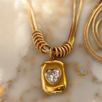 Close-up of double snake chain necklace with heart-shaped zirconia pendant in bold gold frame.
