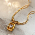 Curved snake chain necklace with heart pendant displayed in soft lighting on warm-toned background.