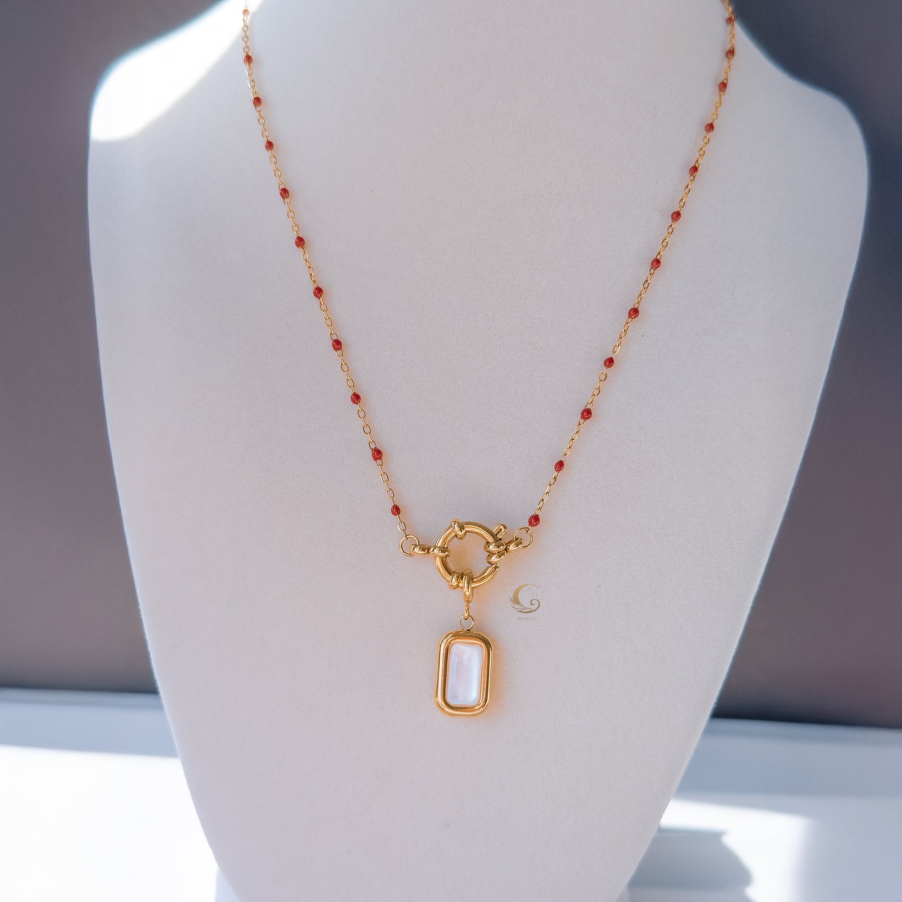 Red beaded necklace with mother of pearl pendant displayed on beige mannequin bust, elegant and minimal background