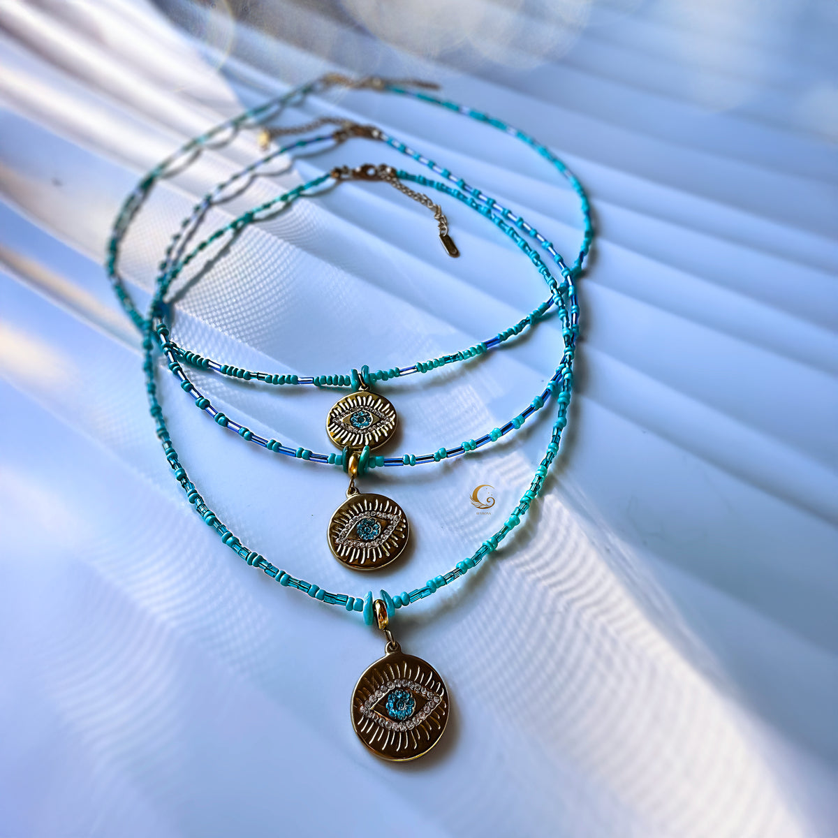 Turquoise beaded necklaces with evil eye pendants on a textured white surface
