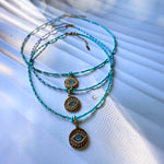 Turquoise beaded necklaces with evil eye pendants on a textured white surface
