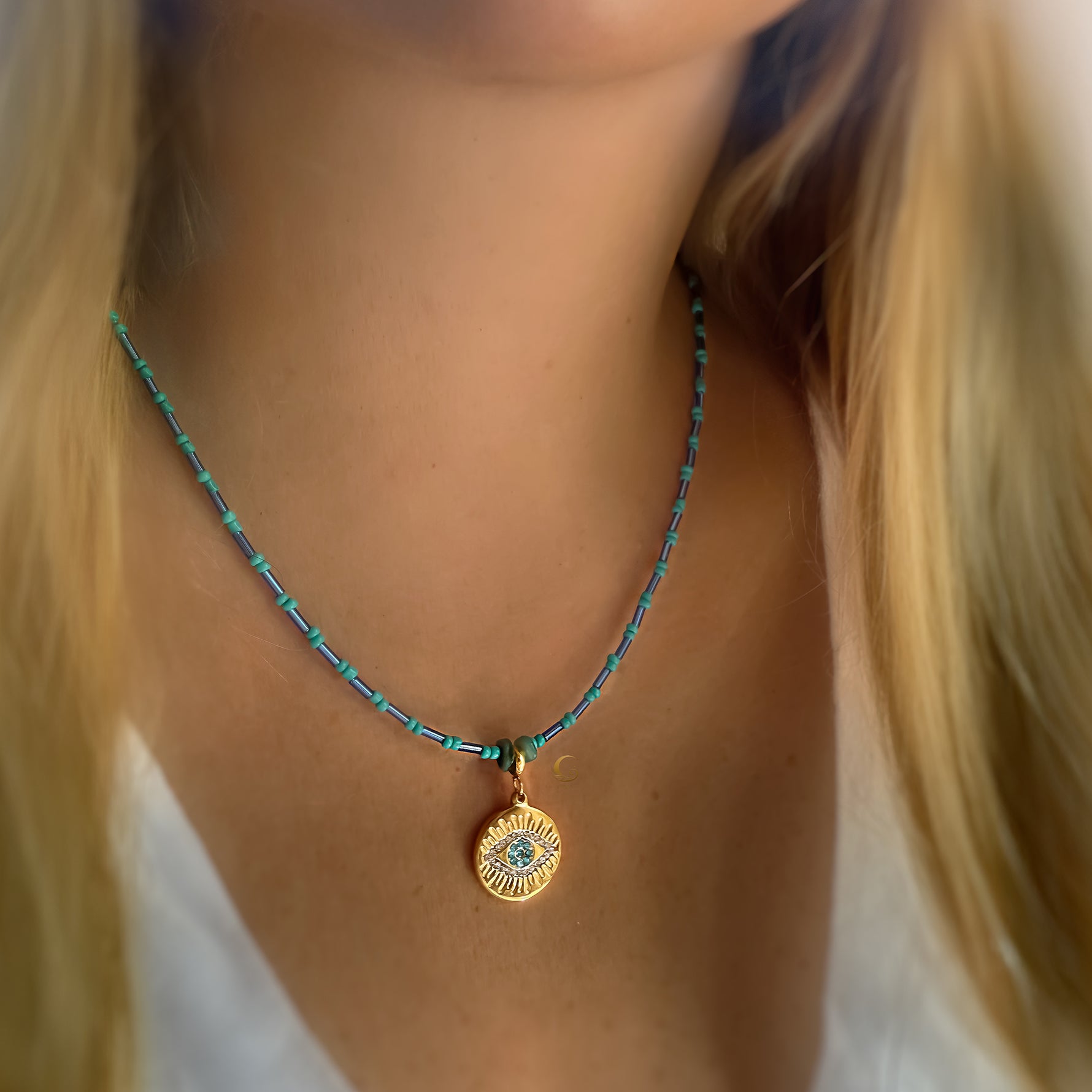 Marisel turquoise Evil Eye necklace worn on model’s neck, featuring gold medallion with zirconia and beaded chain.