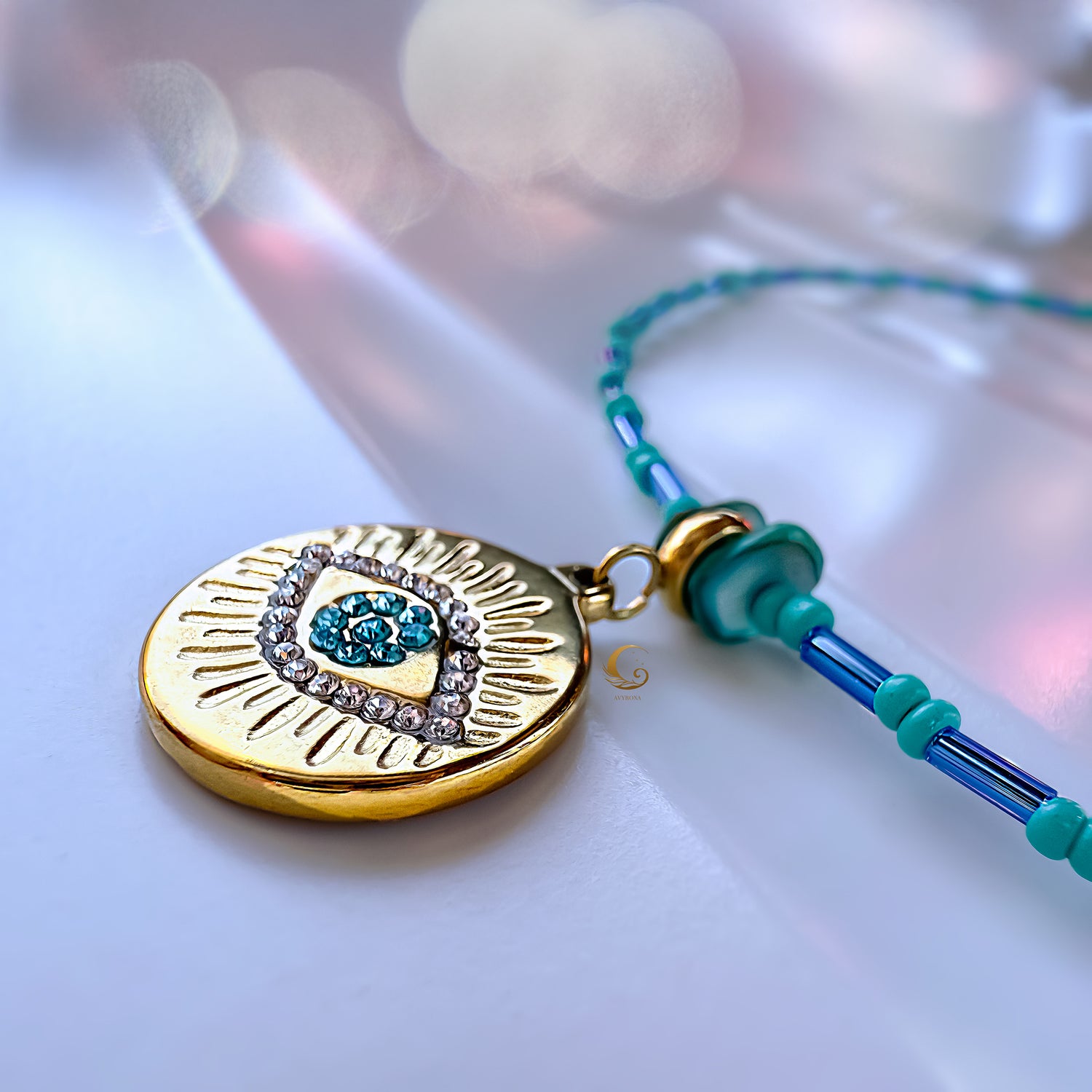 Close-up of the Marisel turquoise Evil Eye necklace showing gold medallion with zirconia and turquoise beaded chain on marble background.