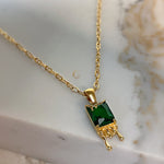 Close-up of Mila necklace showcasing gold honey drip design and emerald green crystal pendant on white marble.