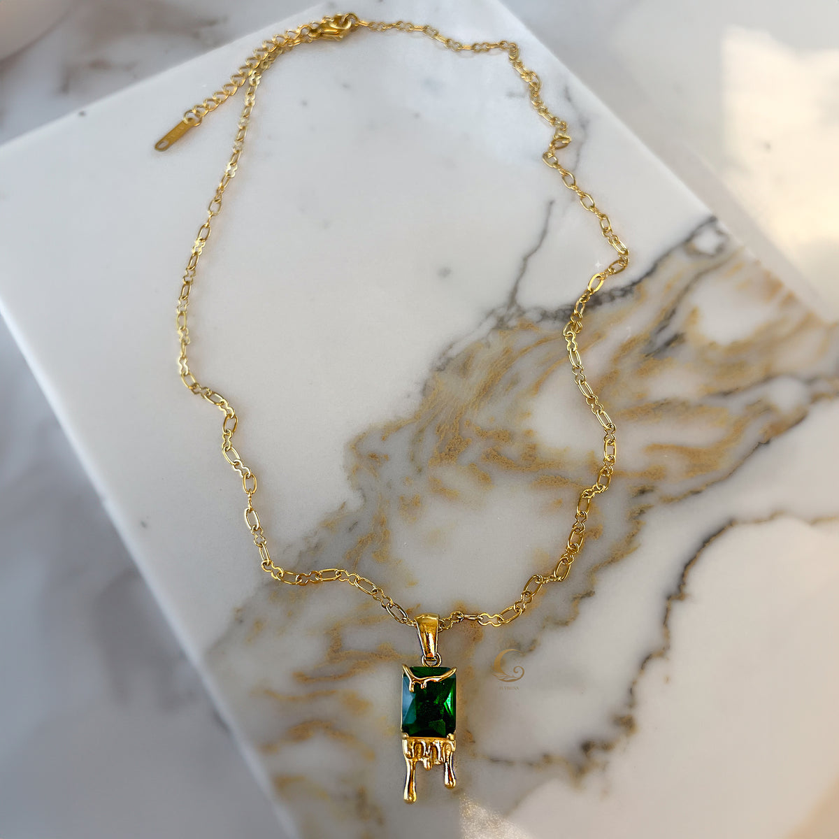 Top-down view of Mila honey drip necklace laid out on marble background, showing entire pendant and delicate gold chain.