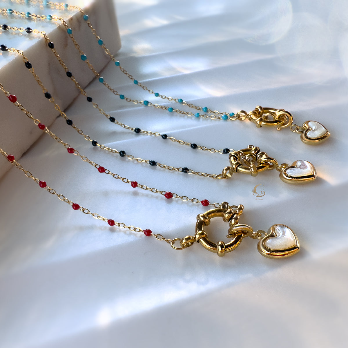  Four heart charm necklaces in different bead colors (red, navy, blue, black), laid out in parallel rows.