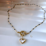  Full view of navy beaded necklace with gold heart charm, displayed in a soft circular shape on white background.