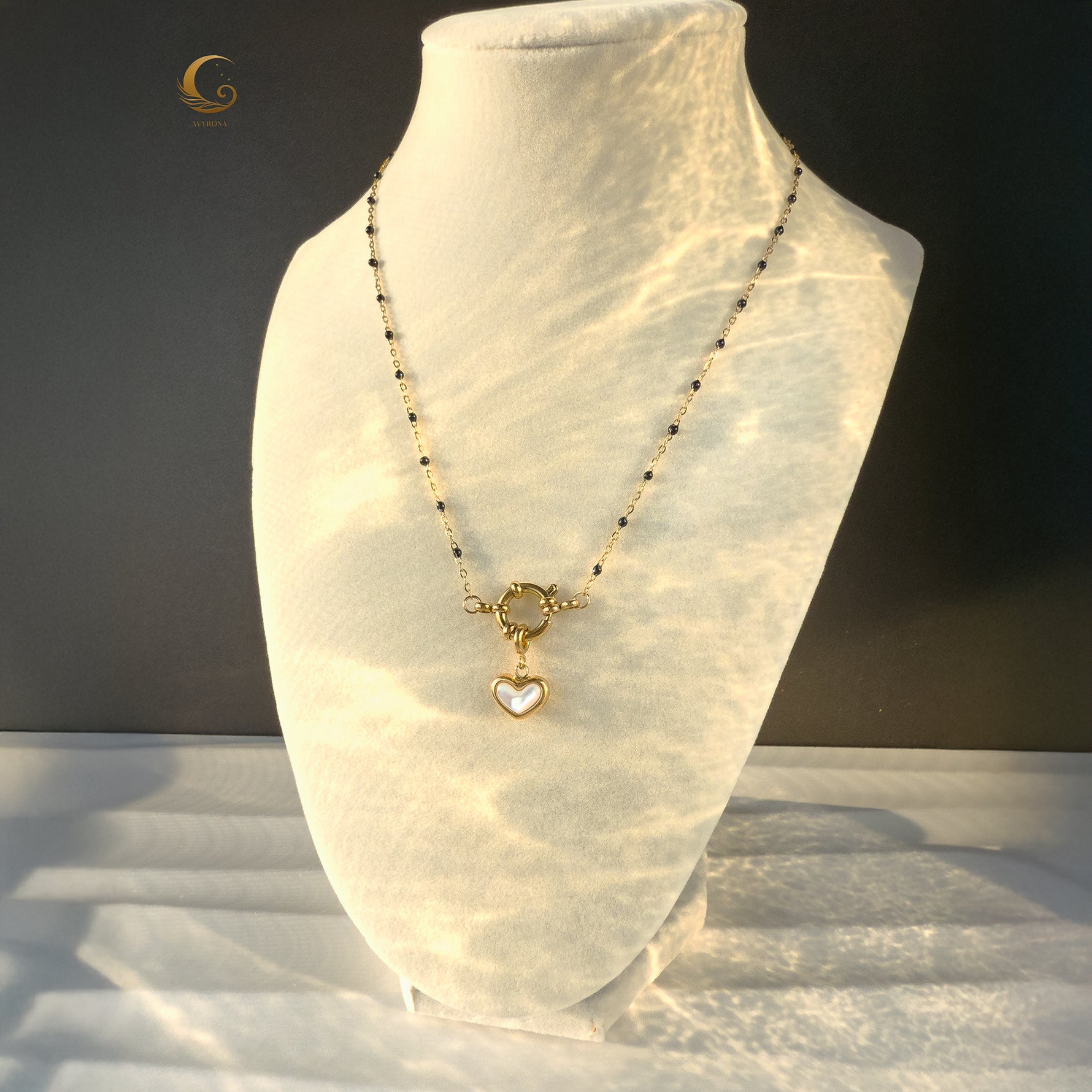 Navy and gold heart necklace shown on white jewelry stand, with wavy light patterns across the display.