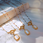 Group of four mother of pearl necklaces with different bead colors: red, light blue, navy blue, and white – arranged on marble block