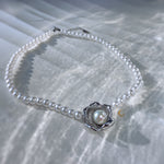 Top view of silver flower pearl necklace on reflective surface