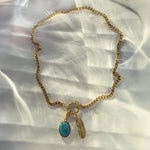 Flat-lay of gold toggle chain necklace with turquoise pendant and feather charm