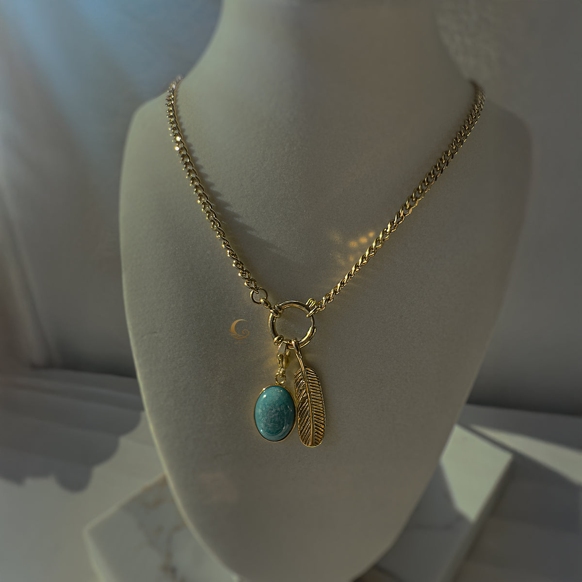 Feather and turquoise pendant necklace on white display bust in warm light