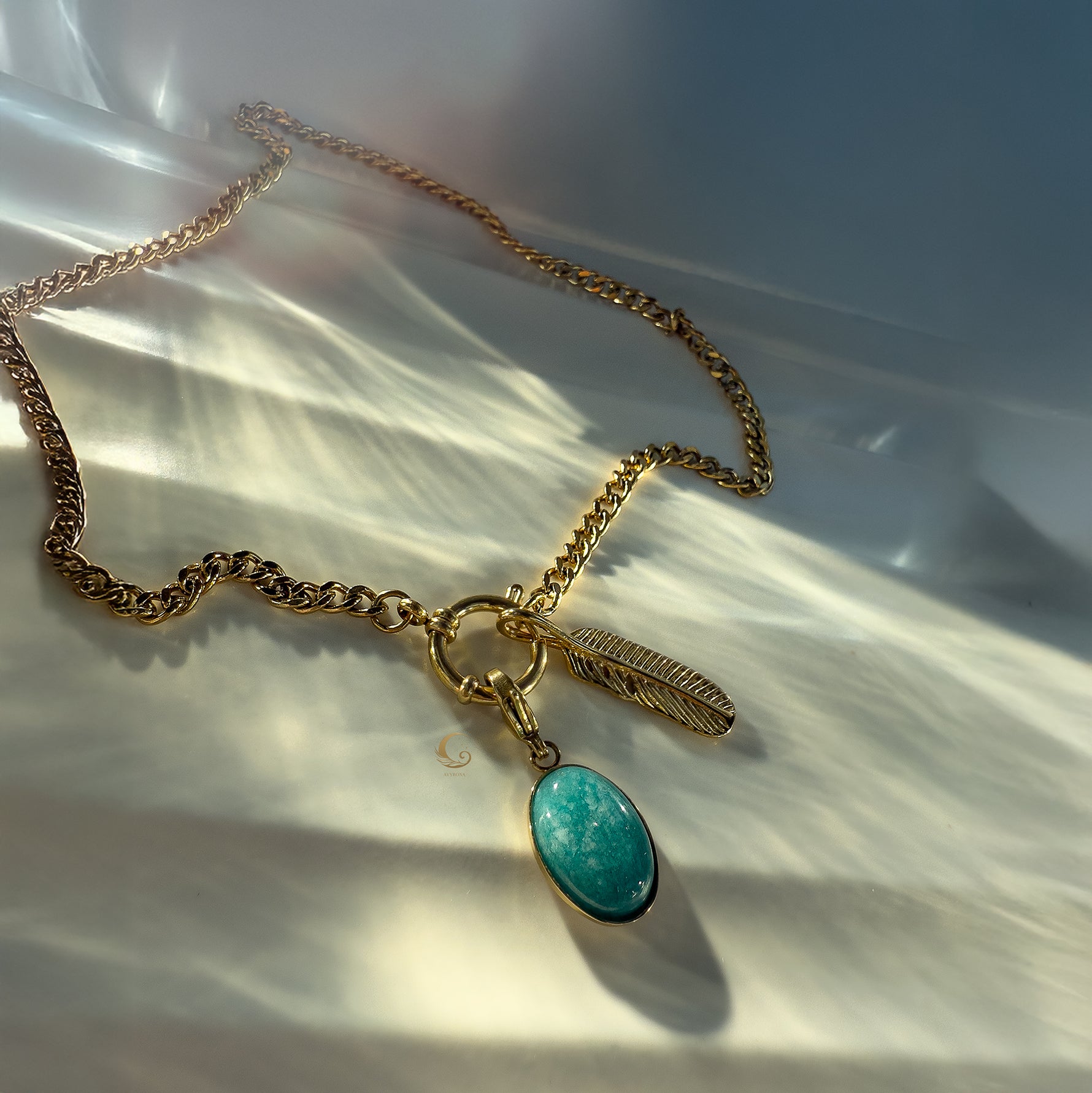  Gold chunky chain necklace with turquoise stone and feather charm displayed on pearly fabric