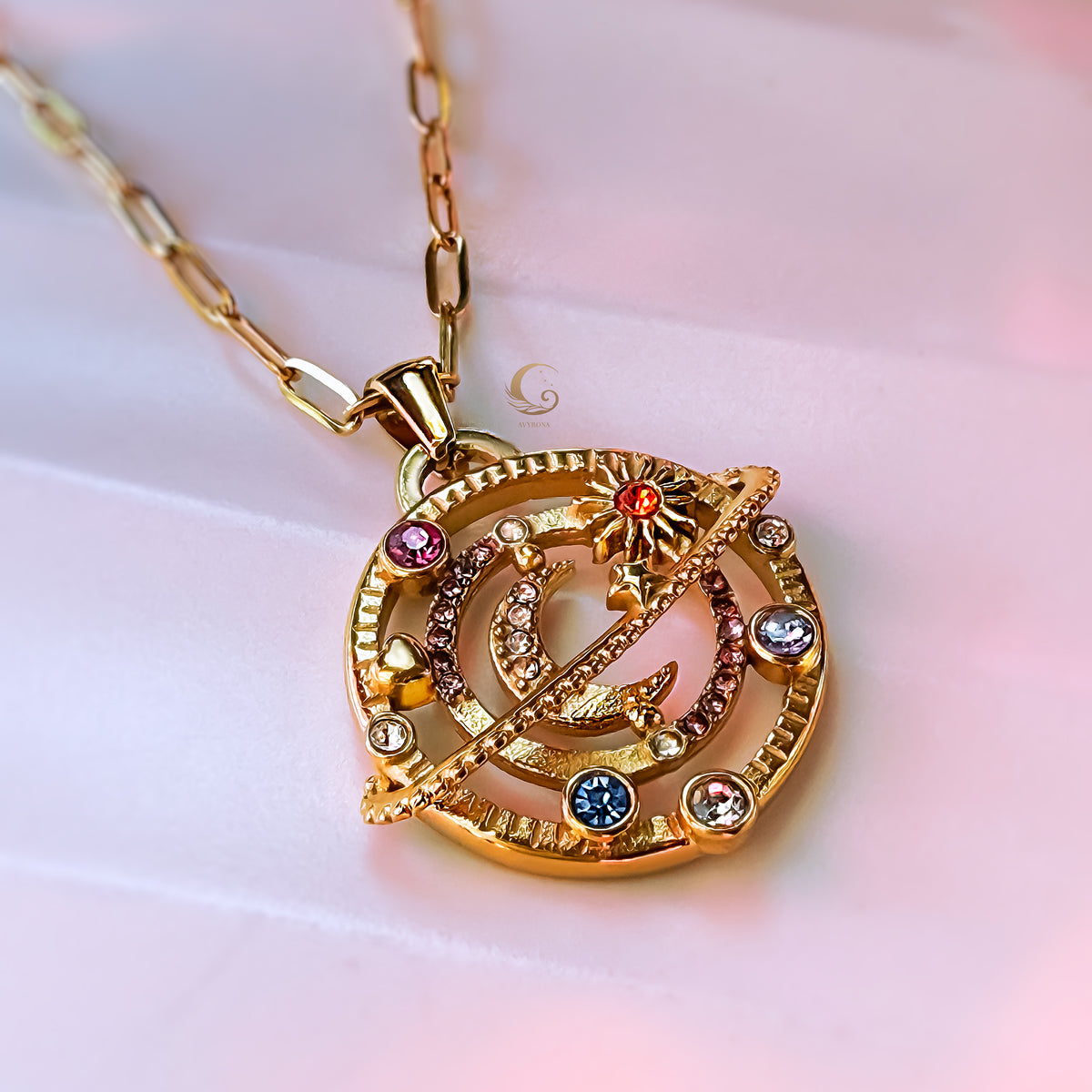 Gold celestial orbit necklace with colorful rhinestones on paperclip chain, photographed on stone-like surface.