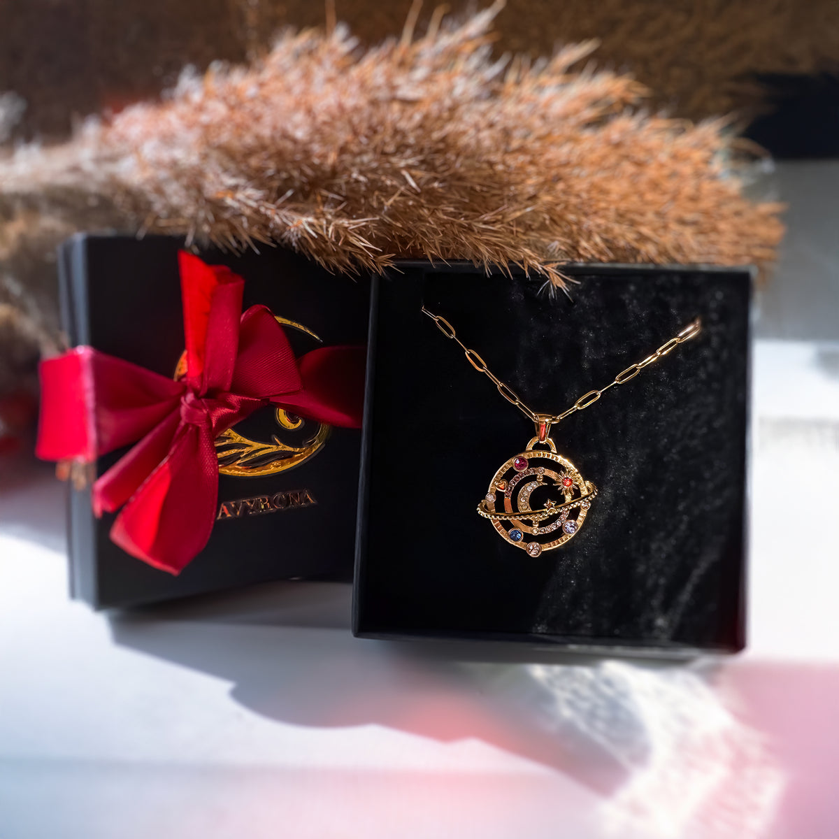 AVYRONA gold orbit necklace in black jewelry box with red ribbon and golden background, gift-ready packaging.