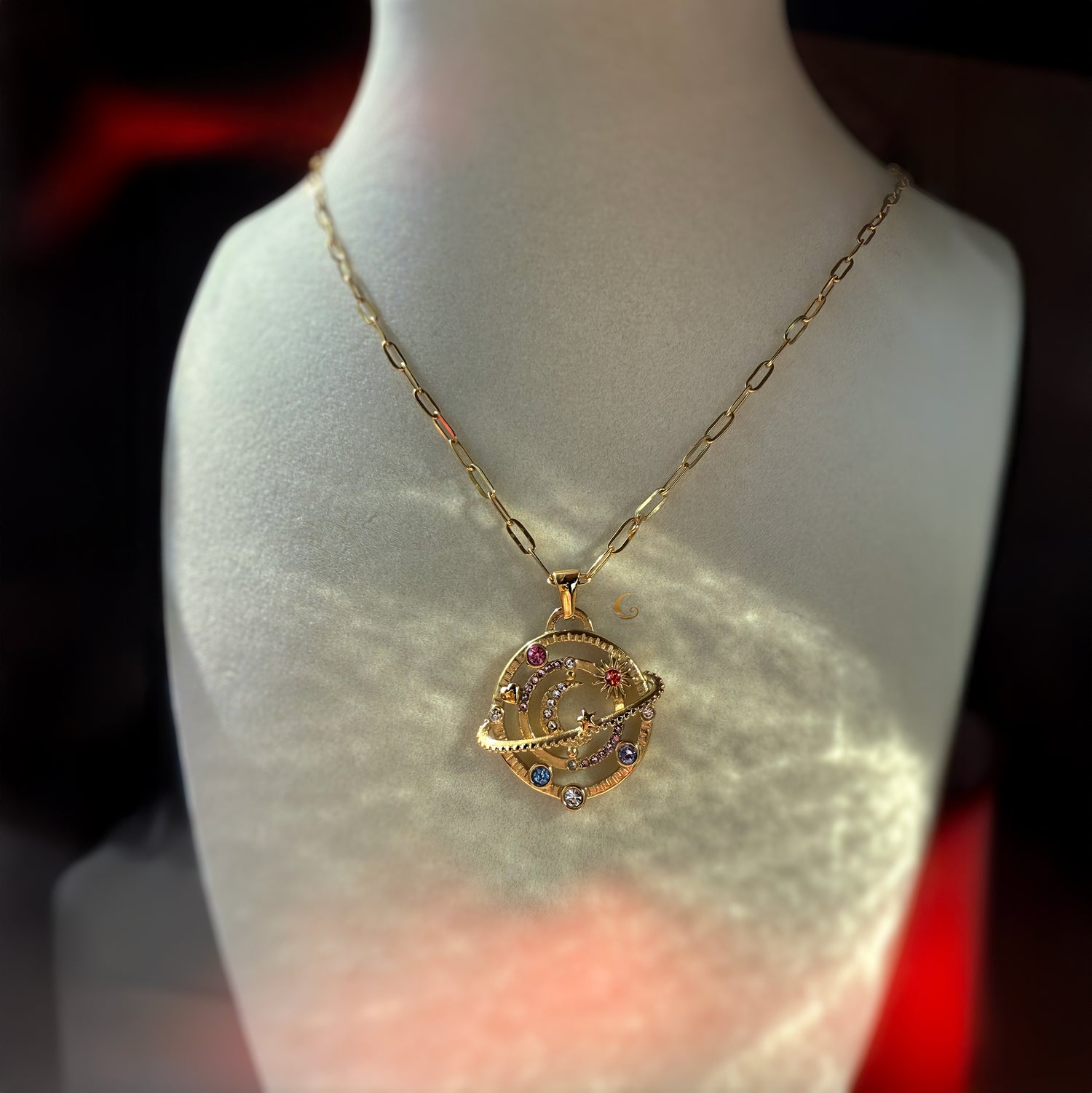 Celestial moon and planet necklace on bust display, gold paperclip chain reflecting warm light.