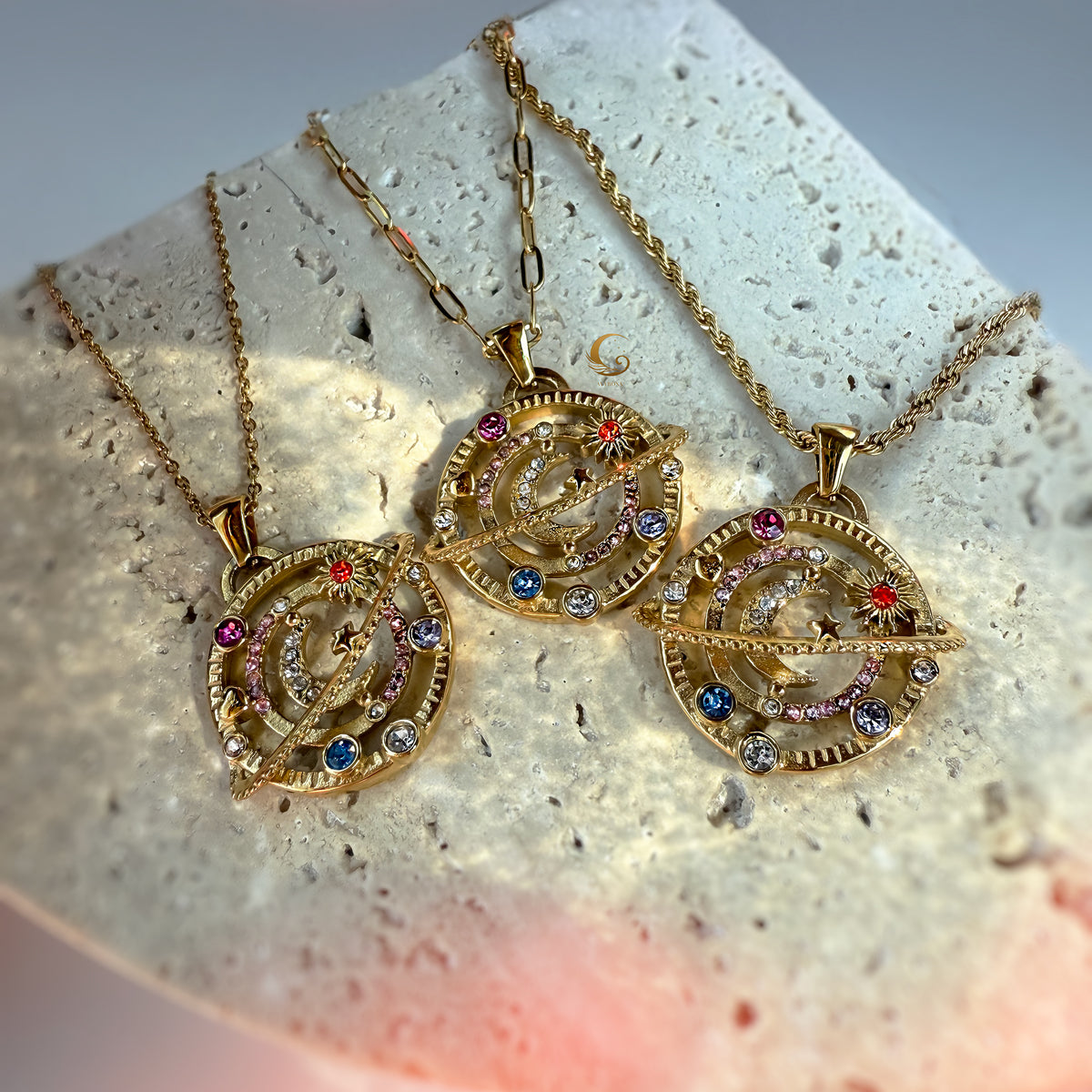 Set of three celestial orbit necklaces on textured stone background, showing link, rope, and paperclip chain styles.