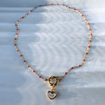 Full view of red beaded necklace with heart pendant arranged in a circular shape on white surface