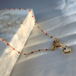 Delicate red beaded necklace with gold toggle clasp and mother-of-pearl heart pendant placed near marble slab