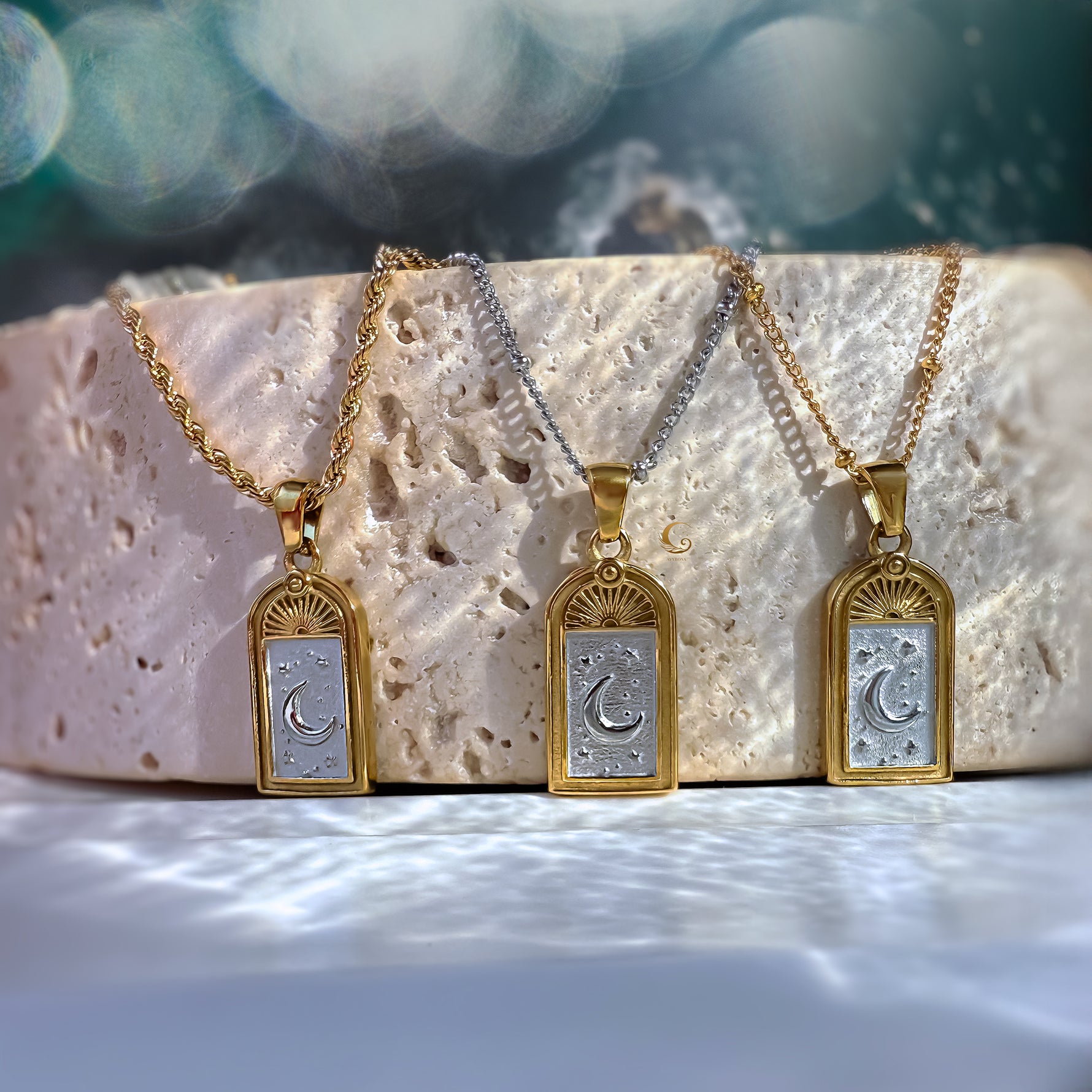Three Selara tarot moon necklaces in gold and silver stainless steel, 18K gold plated, displayed on stone with soft celestial light reflections — Avyrona jewelry.