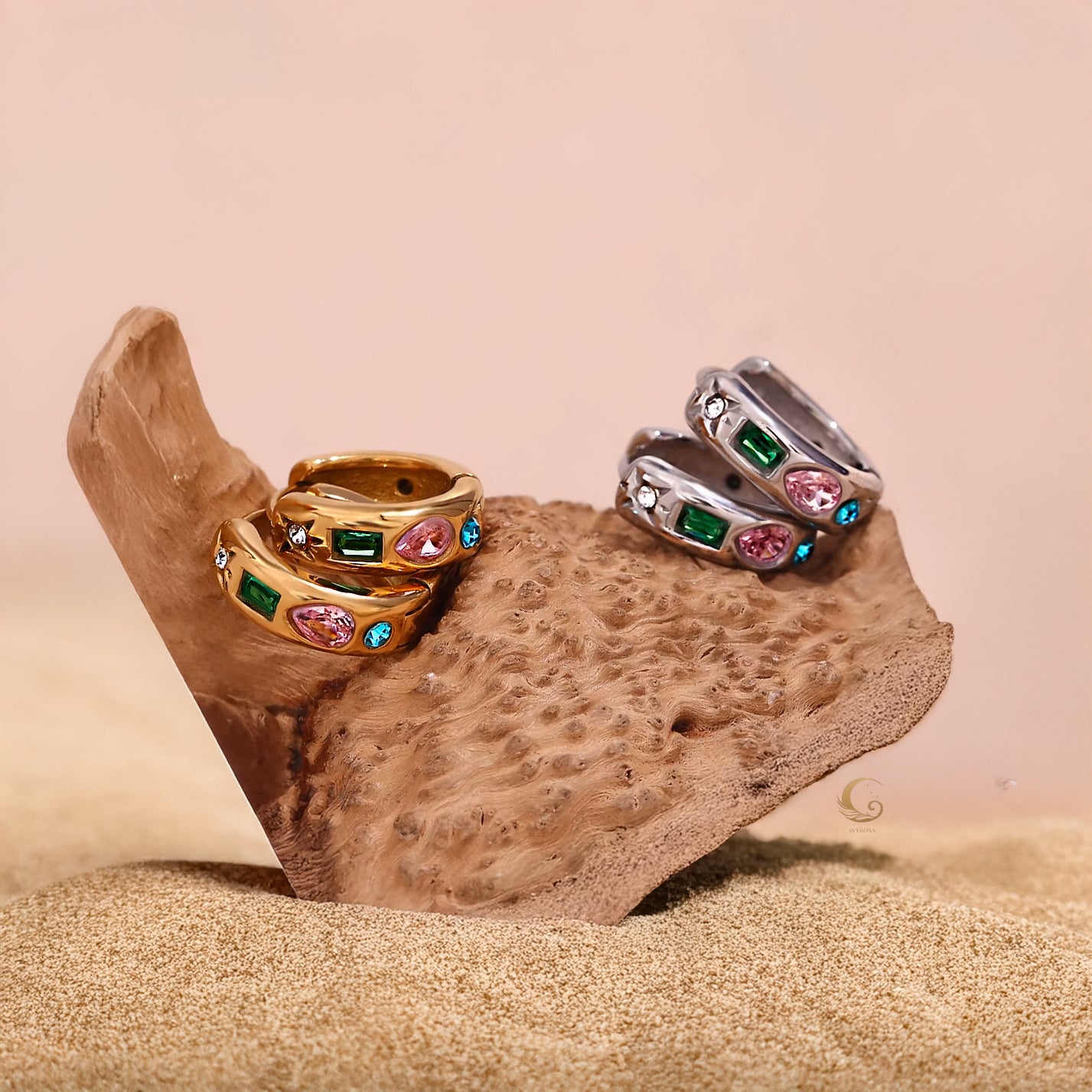 Gold and silver hoop earrings with green, pink, and blue zircon stones displayed on a textured beige rock.