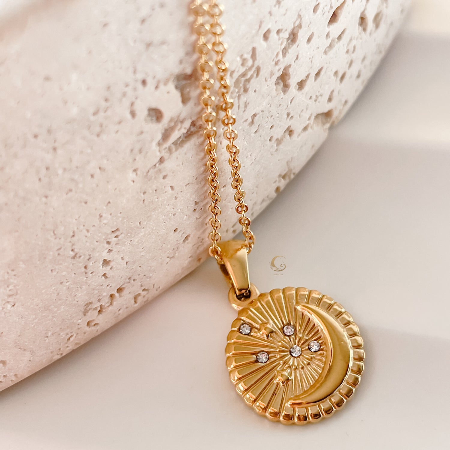 Selene Crescent Moon Necklace displayed flat on a textured surface, featuring gold celestial pendant with fine detailing.