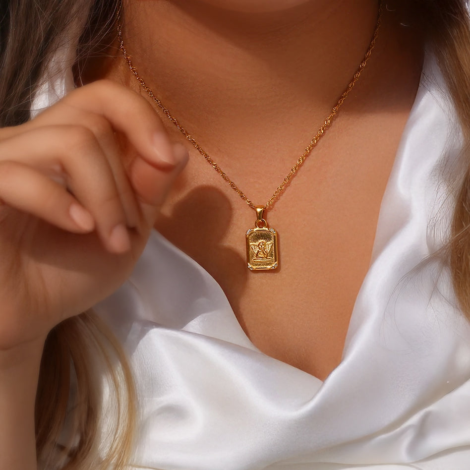 Model wearing the Seraphina angel pendant necklace with shiny gold chain against satin fabric

