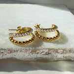 Serina earrings placed on textured stone background, showing layered pearl and gold details