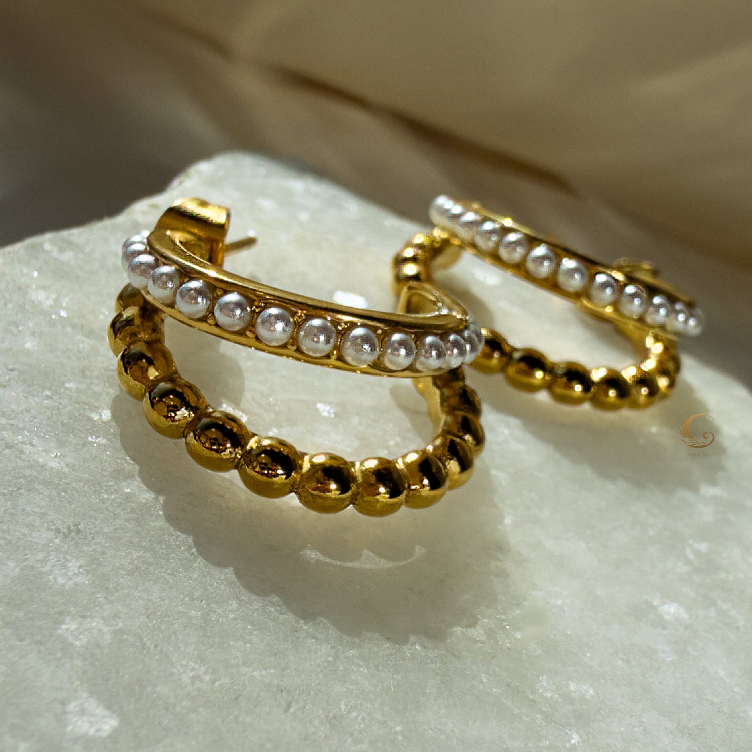 Close-up of Serina gold hoop earrings with pearl-like accents on a satin cream fabric