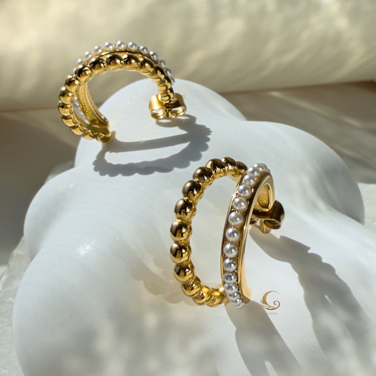 Serina dual hoop earrings displayed on a sculptural white shell with soft morning light