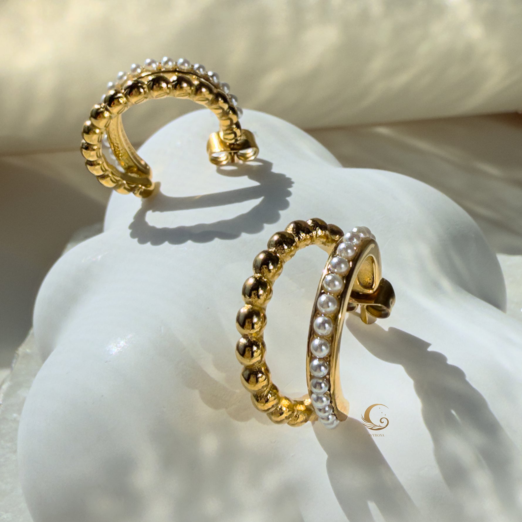 Serina dual hoop earrings displayed on a sculptural white shell with soft morning light