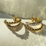 Sparkling view of Serina earrings under golden light, highlighting curved golden spheres and pearl line