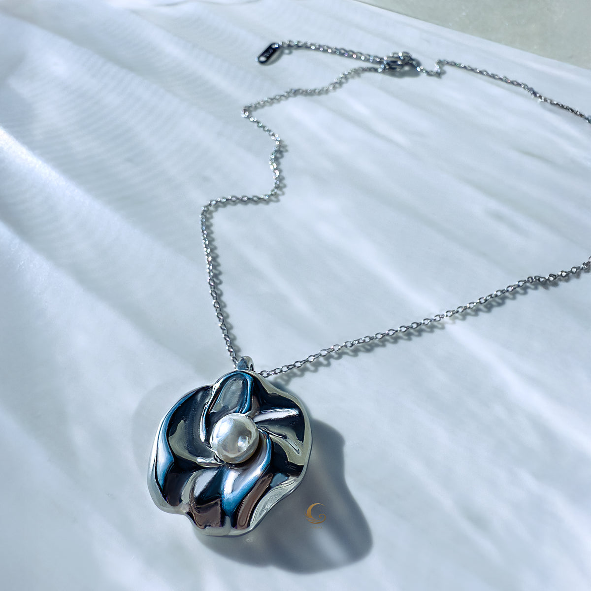 Silver sculpted flower necklace with luminous pearl lying flat on chain