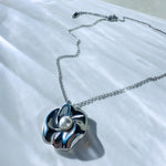 Silver sculpted flower necklace with luminous pearl lying flat on chain
