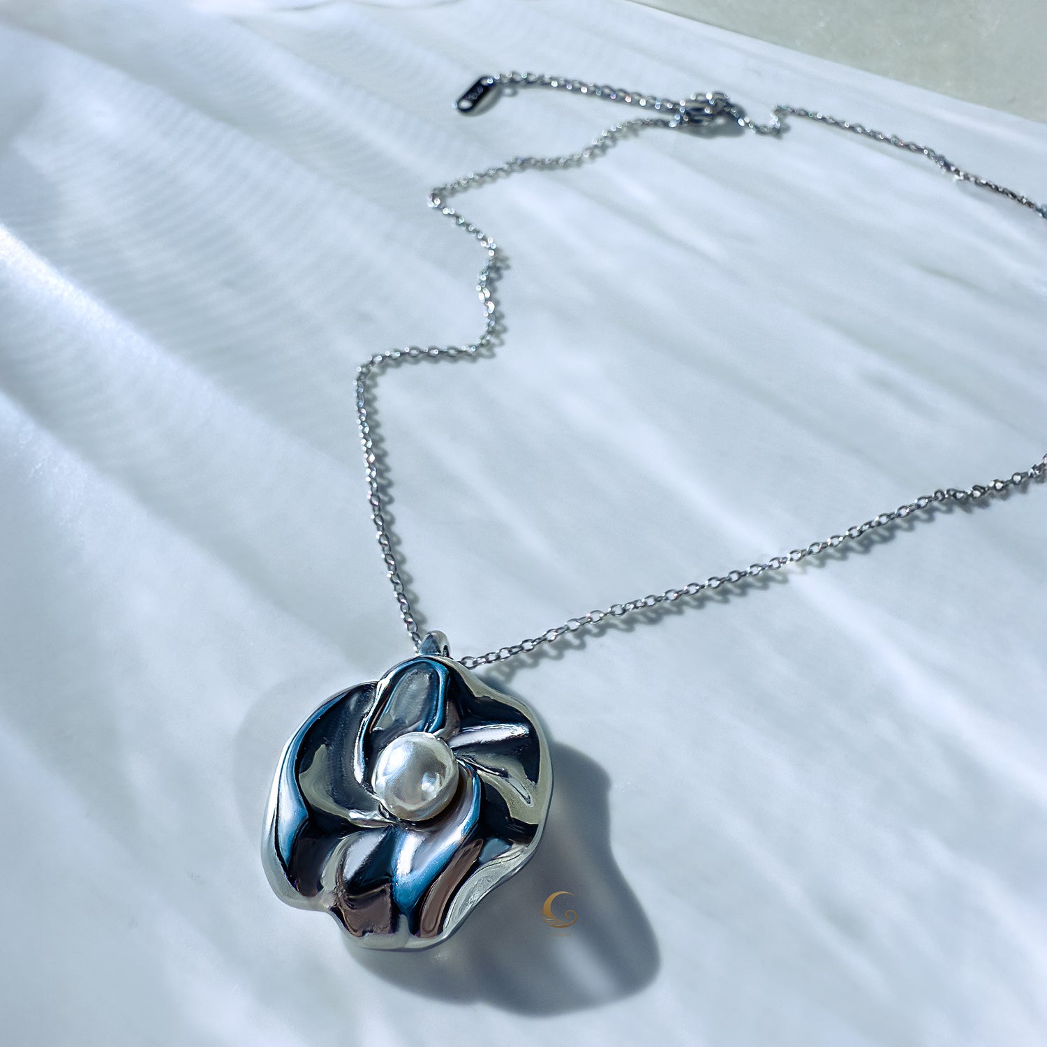Silver sculpted flower necklace with luminous pearl lying flat on chain