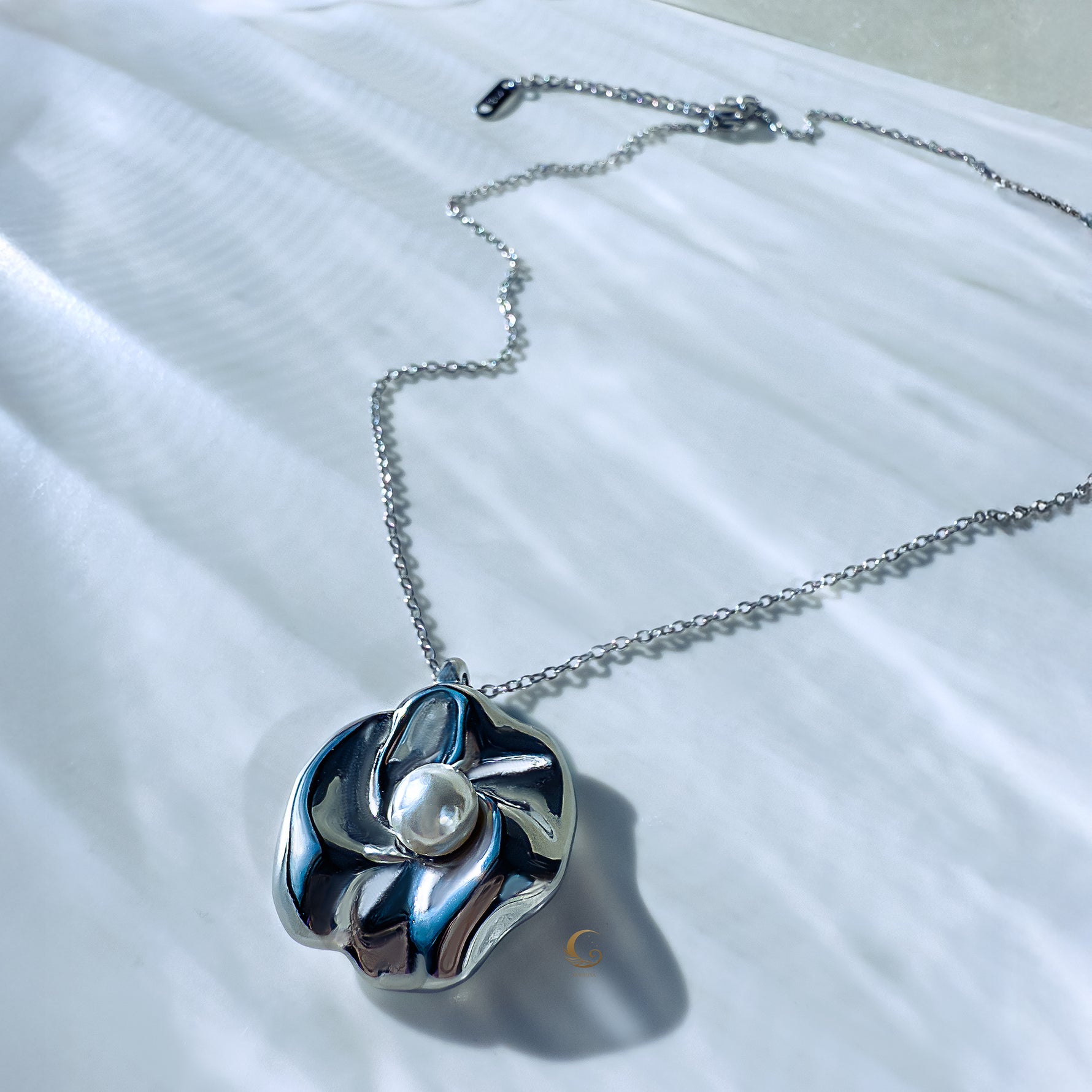 Silver sculpted flower necklace with luminous pearl lying flat on chain