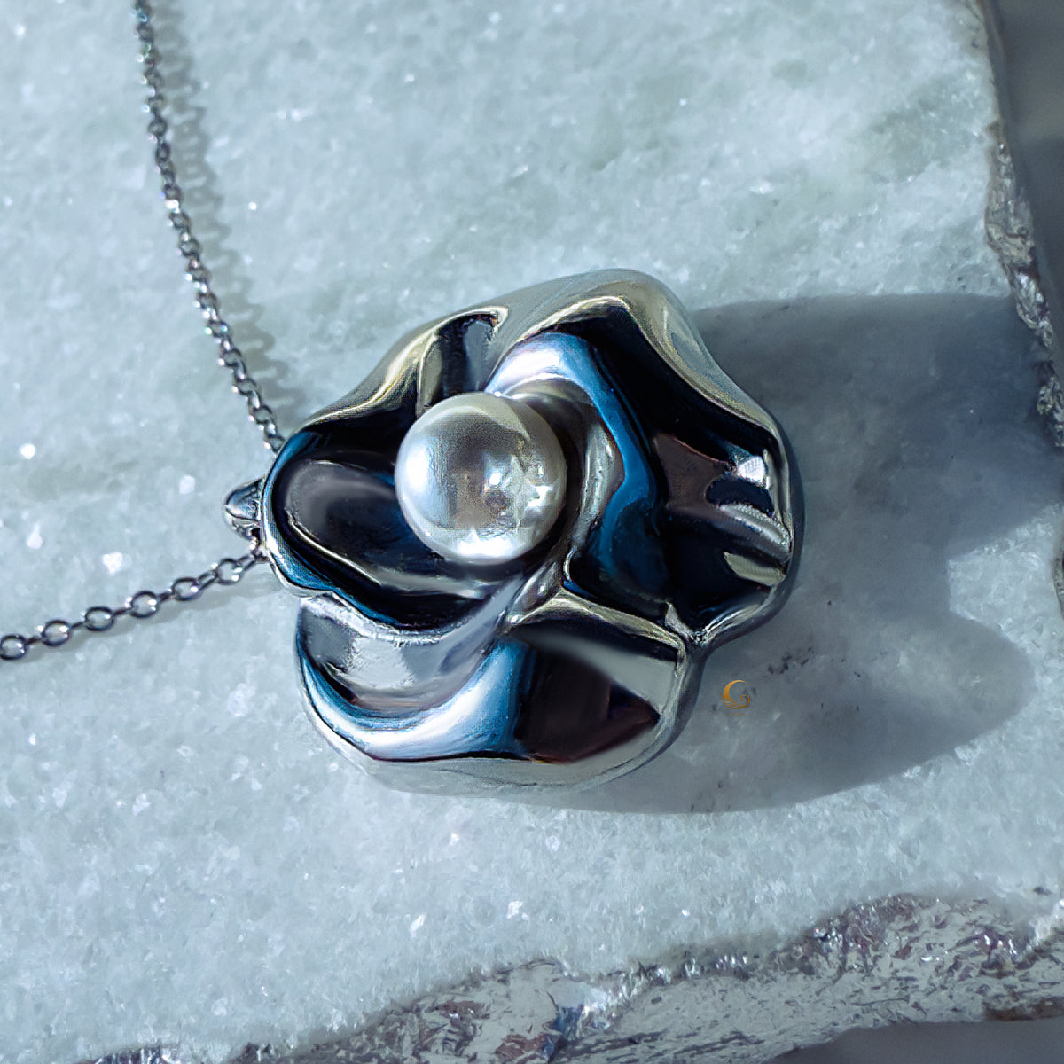 Sculpted silver flower pendant with pearl placed on light natural stone