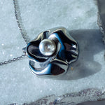 Sculpted silver flower pendant with pearl placed on light natural stone